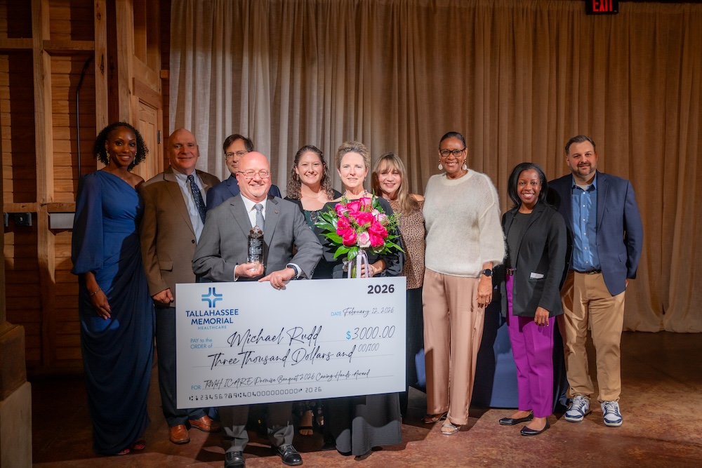 Group of people pose with Caring Hands Award winner as he holds his check