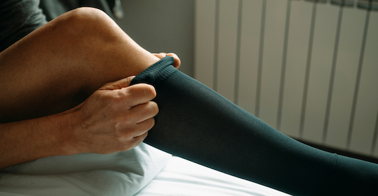 man putting on compression socks while sitting in bed